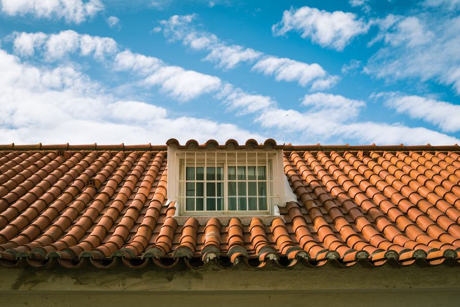 Toit de tuiles terracotta avec une lucarne à petits bois blancs, sous un ciel nuageux